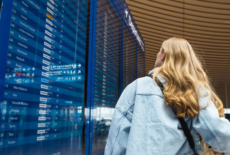 Nainen seisoo lentokentällä infotaulun edessä